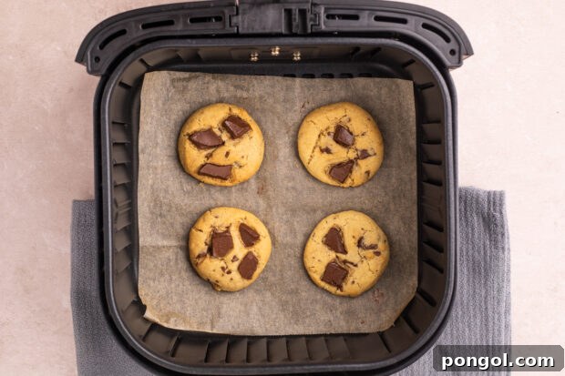 Effortless Air Fryer Chocolate Chip Cookies 8 Overhead view of air fryer chocolate chip cookies on parchment paper in an air fryer basket.