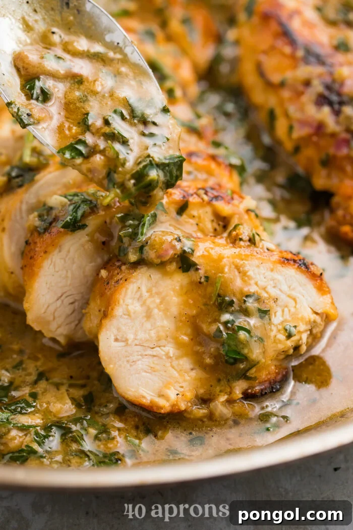 Close-up view of rich garlic herb butter sauce pouring from a spoon onto perfectly sliced, tender chicken breast on a white plate, ready to be served.