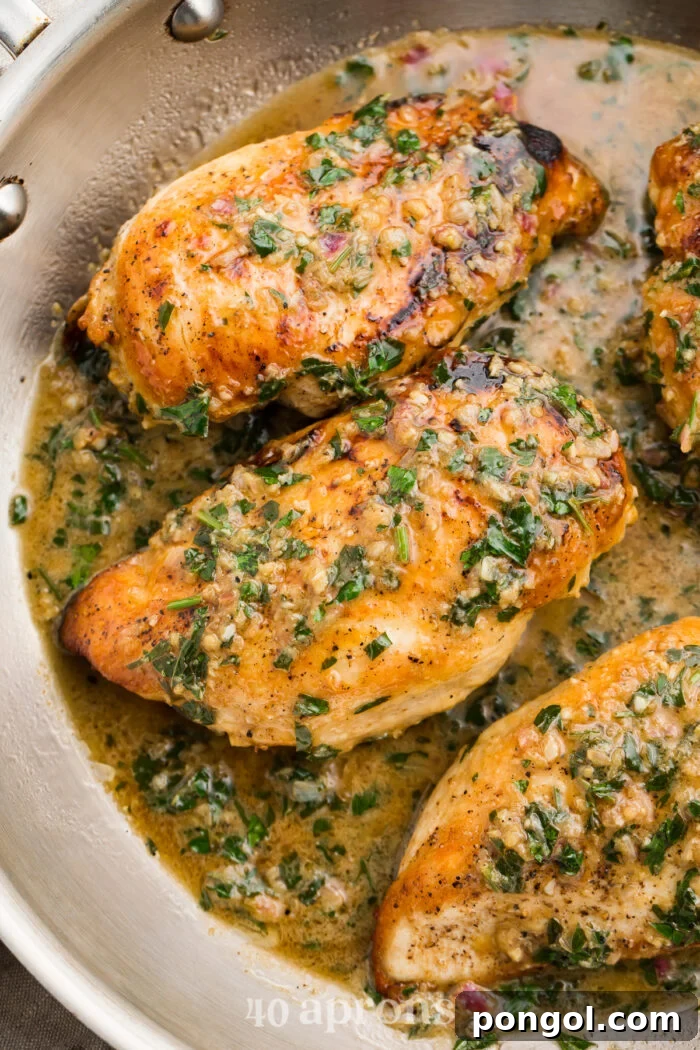 Overhead view of several perfectly seared garlic herb butter chicken breasts simmering in a large silver skillet, coated in the rich sauce.
