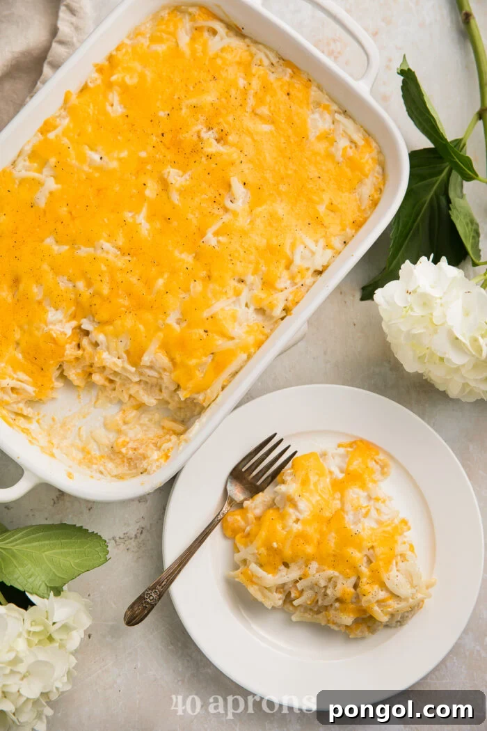 Overhead view of a cheesy copycat Cracker Barrel hashbrown casserole in a casserole dish, with a large scoop of casserole on a plate next to the dish.