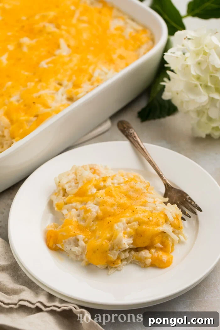 Closer, angled view of a scoop of Cracker Barrel hashbrown casserole topped with cheese on a white plate with a fork.