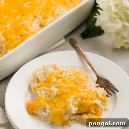 Closer, angled view of a scoop of Cracker Barrel hashbrown casserole topped with cheese on a white plate with a fork.