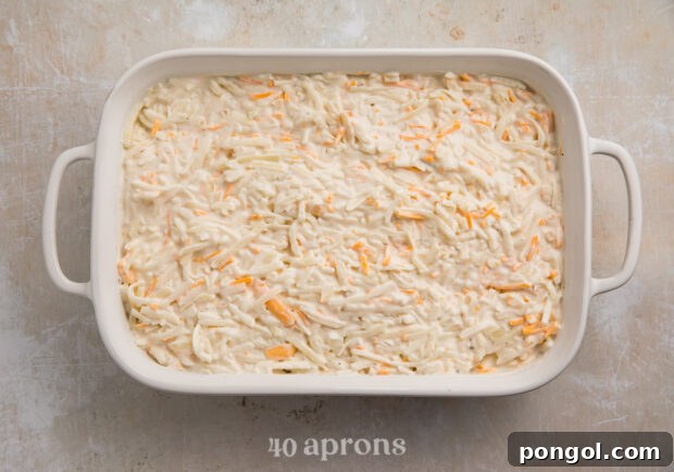 Overhead view of uncooked hashbrown casserole in a large white baking dish with handles.