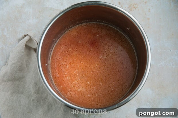 Overhead view of long grain rice, tomato sauce, chicken broth, salt, and cumin in the Instant Pot insert.