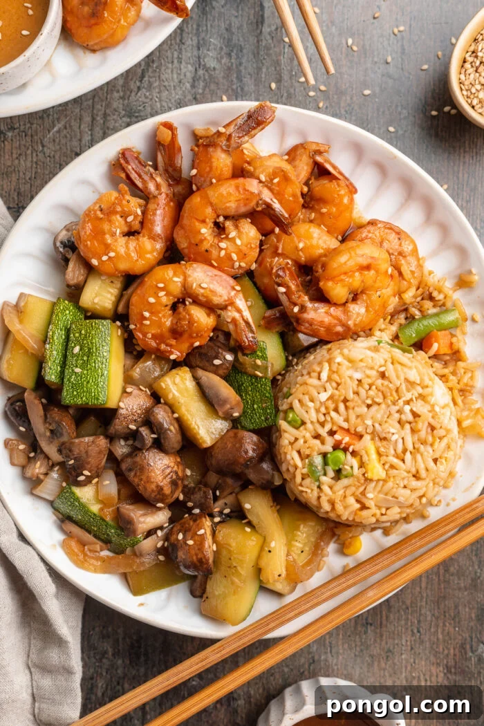 Overhead view of a plate of hibachi shrimp with sautéed veggies, fried rice, and chopsticks.