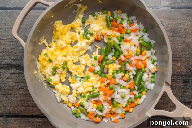 Overhead view of frozen peas and carrots in a large skillet with scrambled eggs.