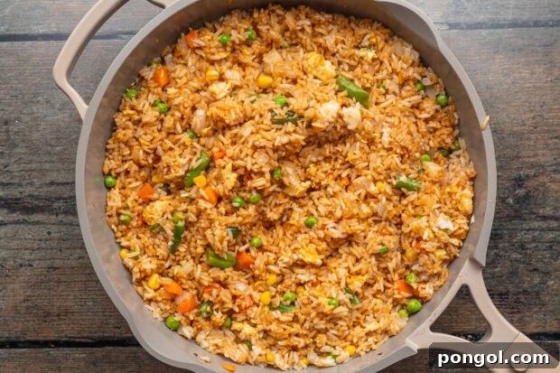 Overhead view of fried rice with peas, carrots, onions, and scrambled eggs in a large grey skillet.