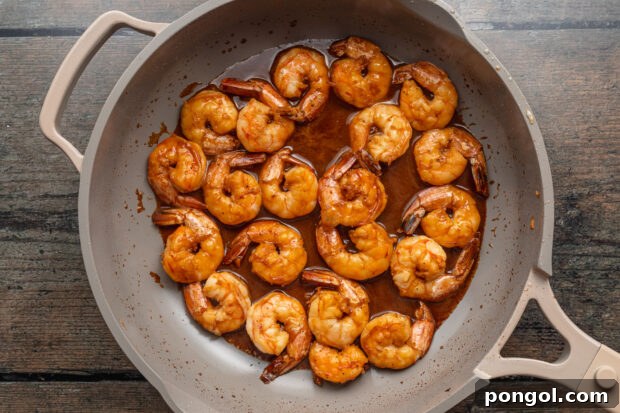 Overhead view of bright orange hibachi shrimp in a large grey skillet on a neutral background.
