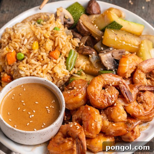 Angled view of hibachi shrimp with fried rice, sautéed vegetables, and a spicy mustard sauce on a plate.