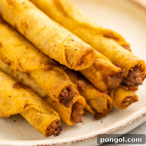 A stack of frozen taquitos cooked in the air fryer then arranged on a white plate in a pyramid-shaped pile, showcasing their golden crispness.