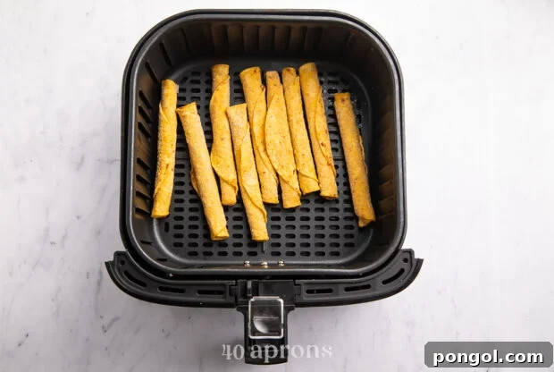 Overhead view of crispy frozen corn taquitos in an air fryer basket on a white countertop, ready for cooking.