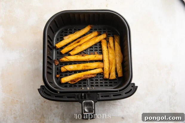Overhead view of crispy cooked taquitos in an air fryer basket resting on a white and grey countertop, perfectly golden and ready to serve.