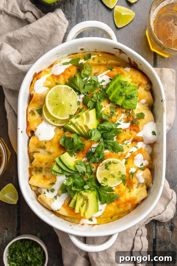 Overhead view of a casserole dish containing shrimp enchiladas topped with cilantro, slices of avocado, and sour cream, ready to be served.