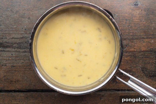 Overhead view of an enchilada cream sauce with melted cheese, green chilis, sour cream, and chicken stock in a medium saucepan.