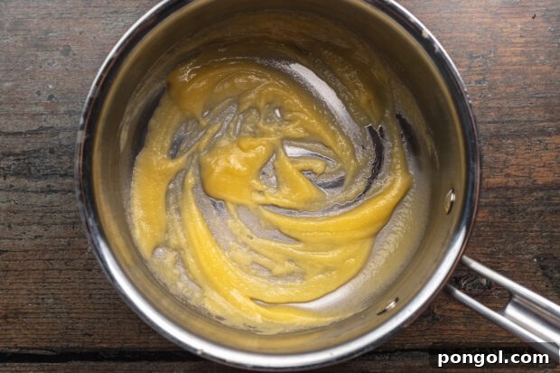 Overhead view of melted butter being whisked with flour in a saucepan to create a roux for the sauce.