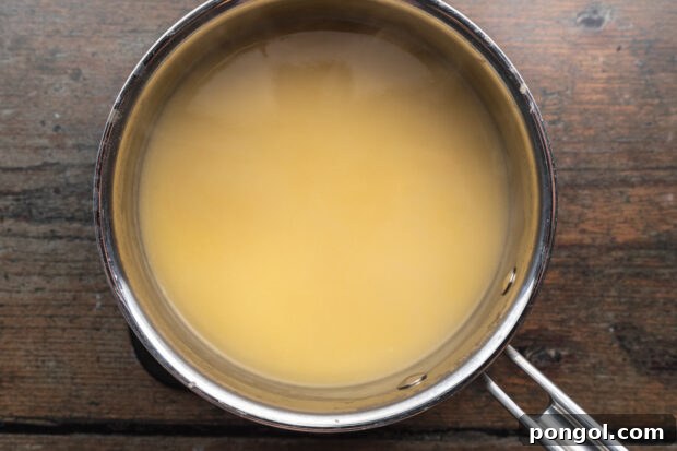 Overhead view of a roux with chicken broth in a medium saucepan, thickening on a neutral background.