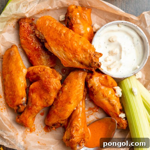 Overhead view of a plate piled high with orange chicken drumsticks and flats, next to a small ramekin of ranch dressing.