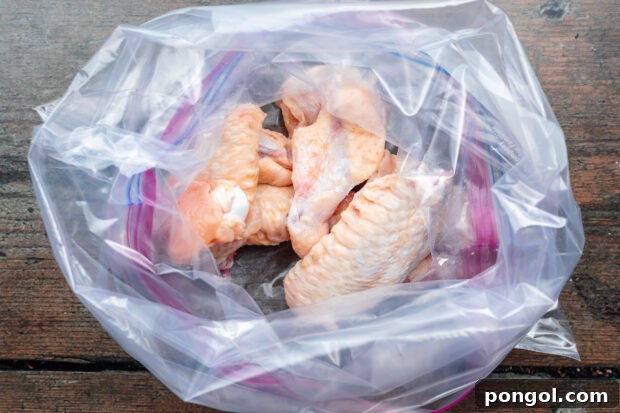 Overhead view of uncooked chicken wings in a large ziploc bag on a dark wooden tabletop.