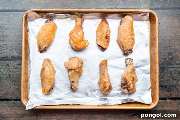 Overhead view of sous vide cooked chicken wings on a baking sheet lined with aluminum foil after the wings go under the broiler.