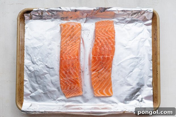 Overhead view of two salmon fillets on a baking sheet lined with aluminum foil.