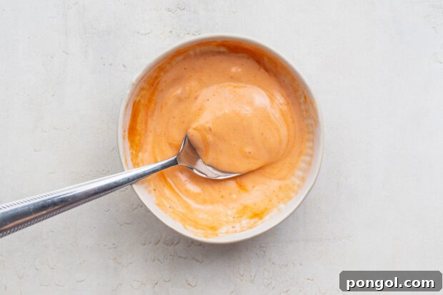 Overhead view of prepared sriracha mayo in a white bowl with a silver spoon.