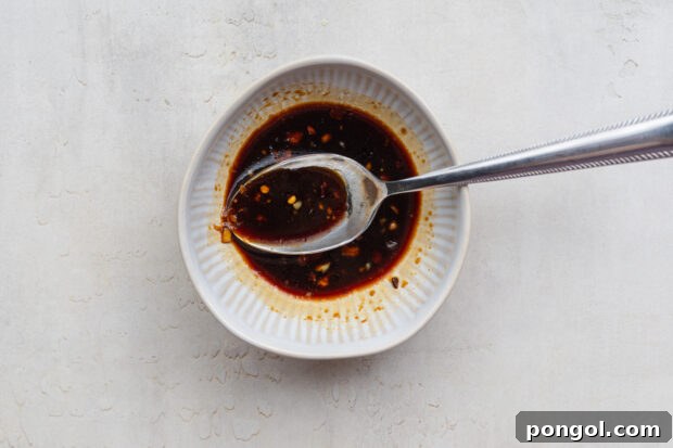 Overhead view of a ginger-garlic soy sauce mixture in a white bowl with a silver spoon.