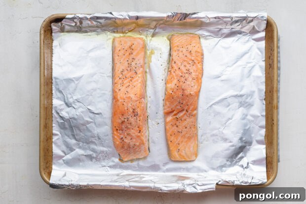 Overhead view of two fully-baked salmon fillets on a baking sheet lined with aluminum foil.