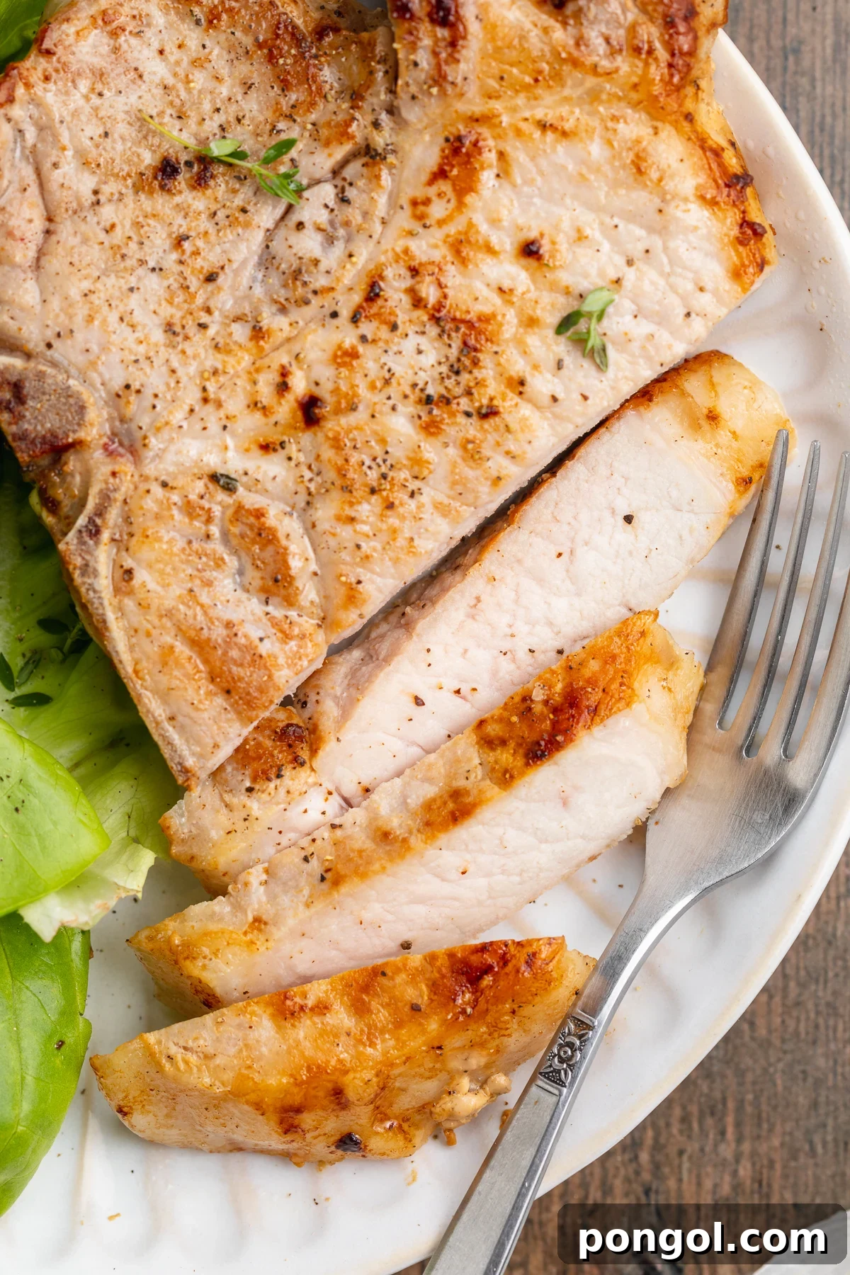 Perfectly Tender Sous Vide Pork Chops 3 Overhead view of a sliced sous vide pork chop on a white plate with a simple green lettuce salad.
