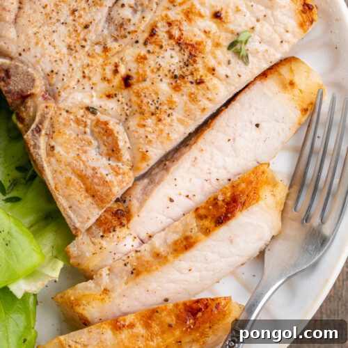 Overhead view of a sliced sous vide pork chop on a white plate with a simple green lettuce salad.