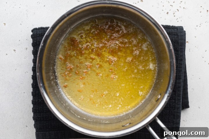 Overhead view of a small silver saucepan with melted butter on an electric burner.
