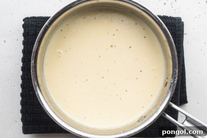 Overhead view of creamy, thick alfredo sauce with heavy cream, parmesan, and asiago cheese in a silver saucepan.
