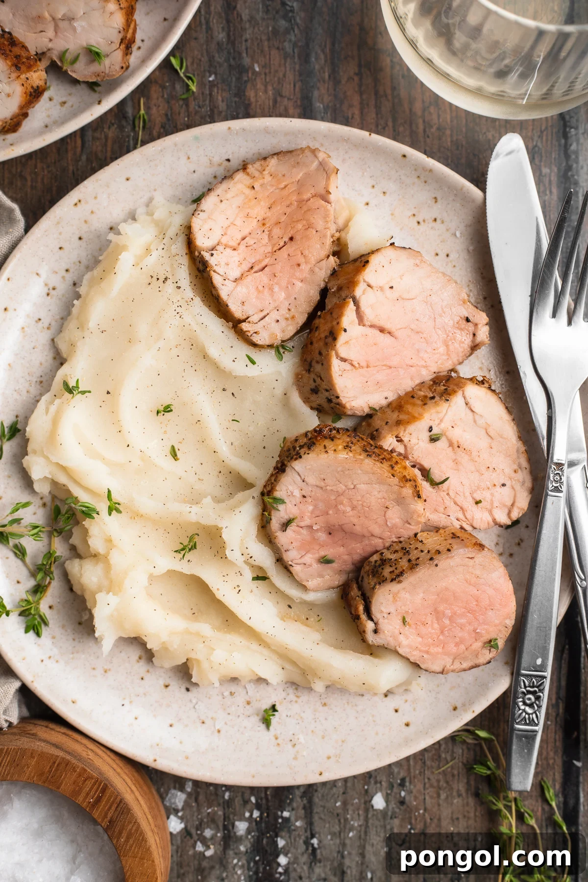 Overhead view of sous vide pork tenderloin sliced and plated with fluffy mashed potatoes on a wooden table.