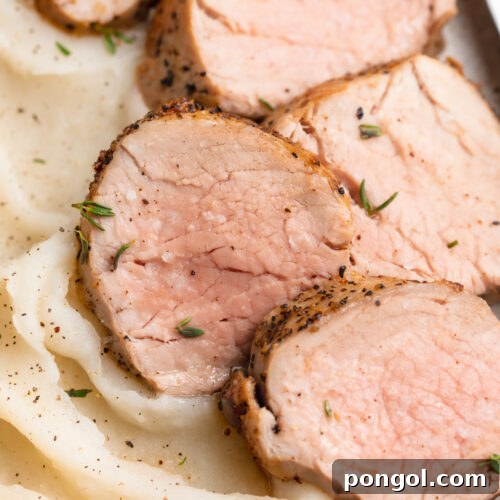 Sliced sous vide pork tenderloin on a white plate with a bed of fluffy whipped mashed potatoes.