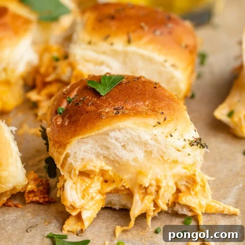 Side view, close up on one buffalo chicken slider, overflowing with melty cheese and shredded buffalo chicken.