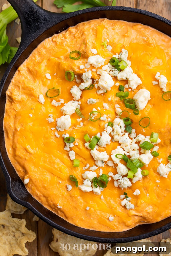 Overhead view of Instant Pot buffalo chicken dip in a cast-iron skillet. Dip is topped with blue cheese crumbles and green onions.
