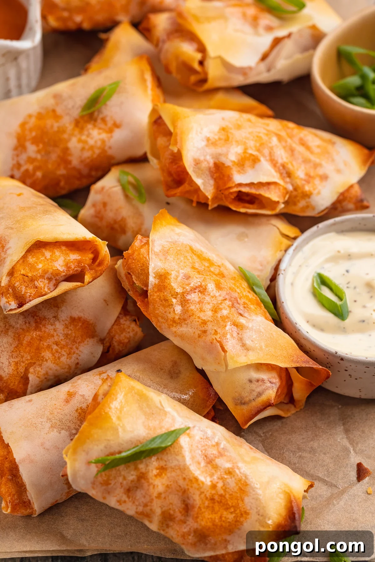 Overhead view of buffalo chicken egg rolls on a sheet of parchment paper next to a ramekin of ranch dressing.