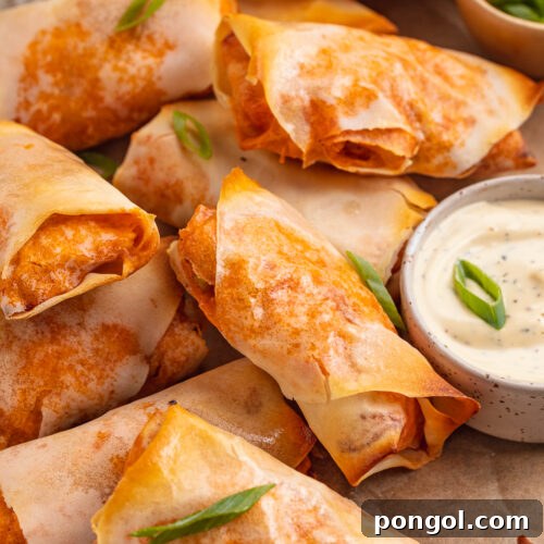 Overhead view of buffalo chicken egg rolls on a sheet of parchment paper next to a ramekin of ranch dressing.