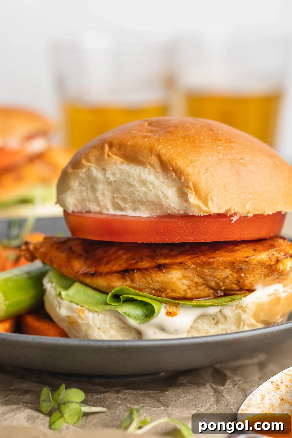 Zesty Buffalo Chicken Stack 2 A tantalizing side view of a buffalo chicken sandwich, featuring a golden-orange pan-seared chicken breast, a thick slice of ripe red tomato, fresh green lettuce, and a perfectly toasted fluffy bun, all served elegantly on a blue-grey plate.