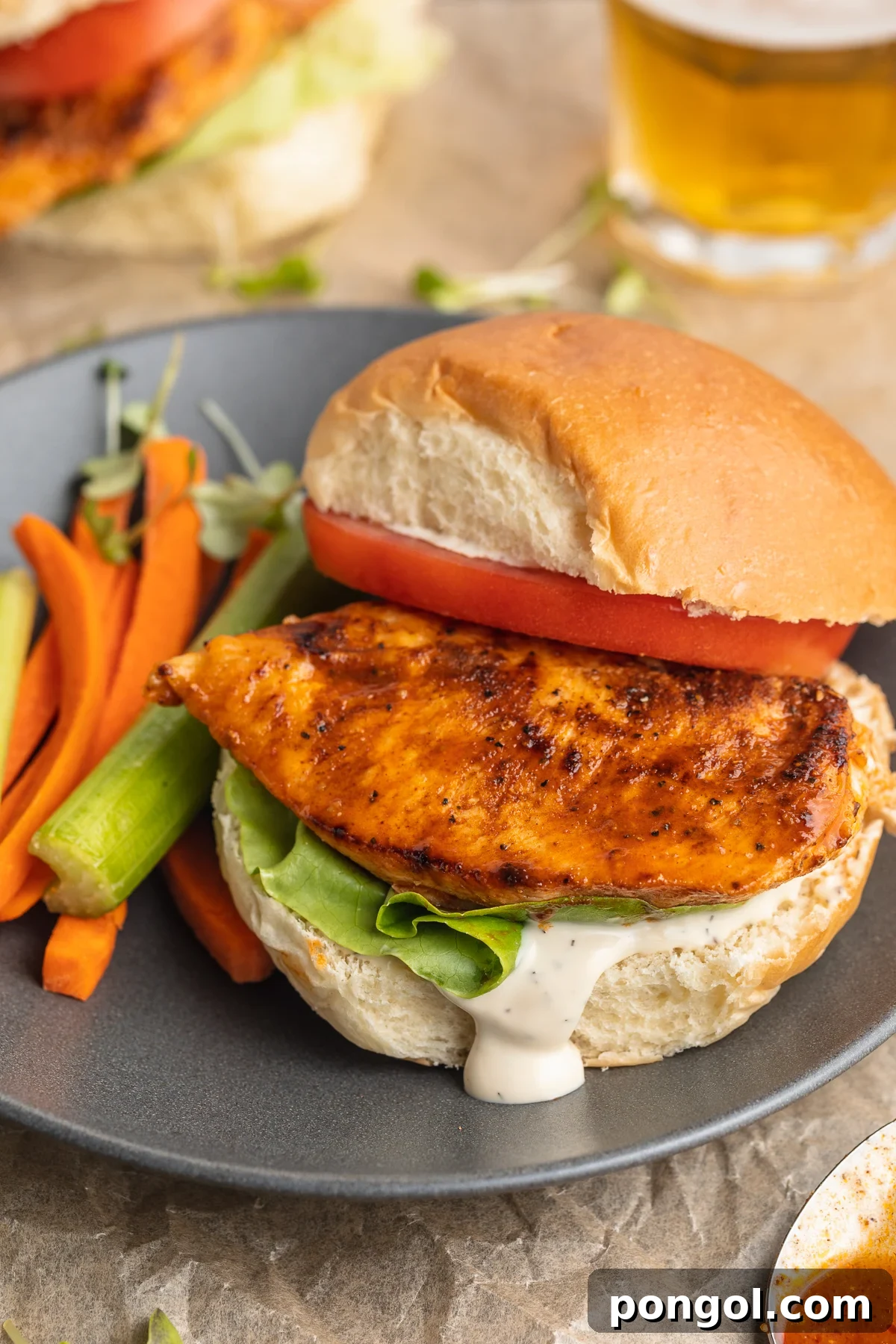Zesty Buffalo Chicken Stack 3 An overhead, slightly angled view captures a buffalo chicken sandwich on a plate. The top bun is gently askew, revealing a generous slice of tomato, fresh lettuce, and the vibrant buffalo-coated chicken beneath, inviting you to take a bite.
