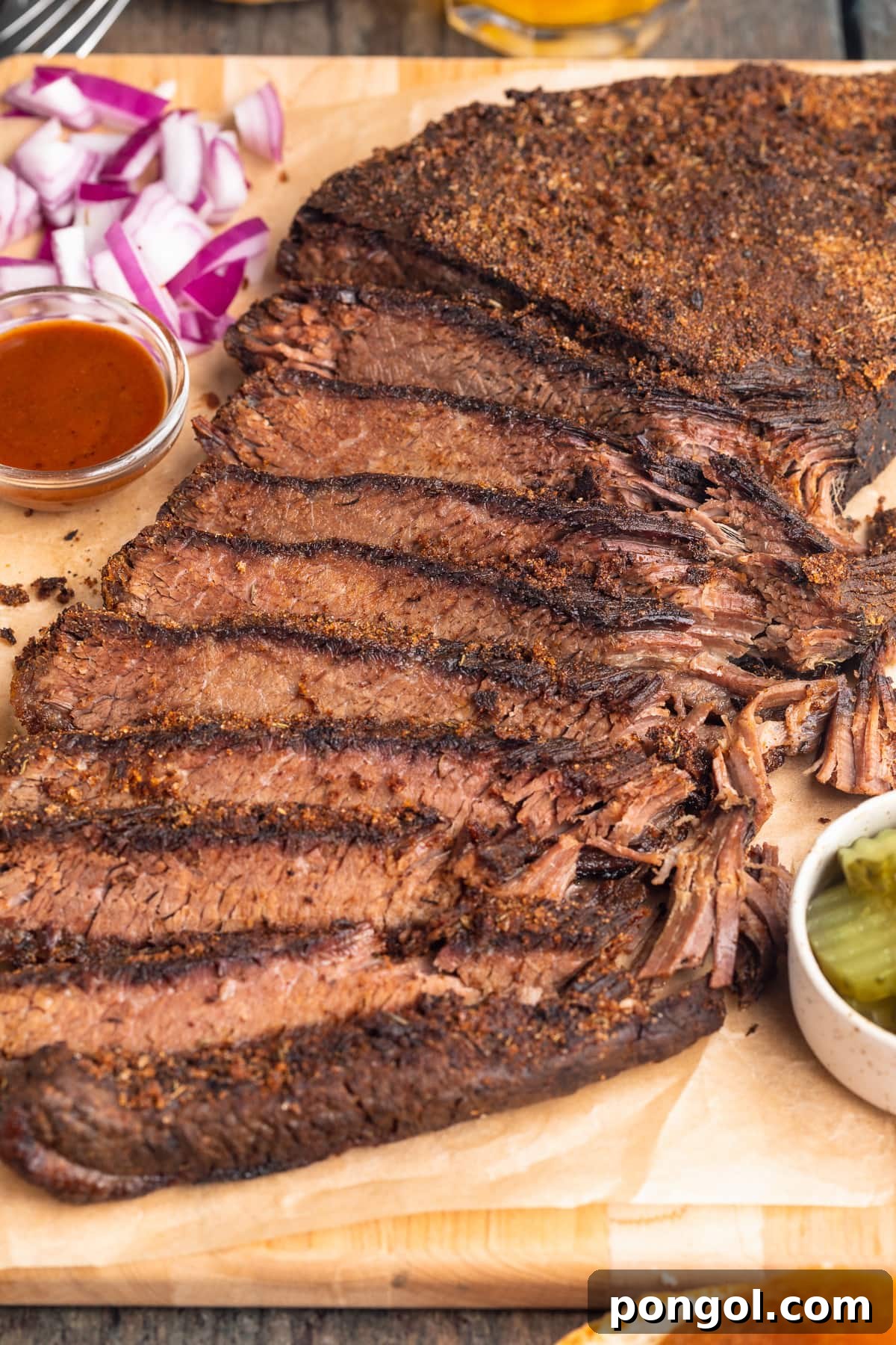 Sous vide brisket, sliced thin and arranged on a wooden serving tray with seasoning and garnish.