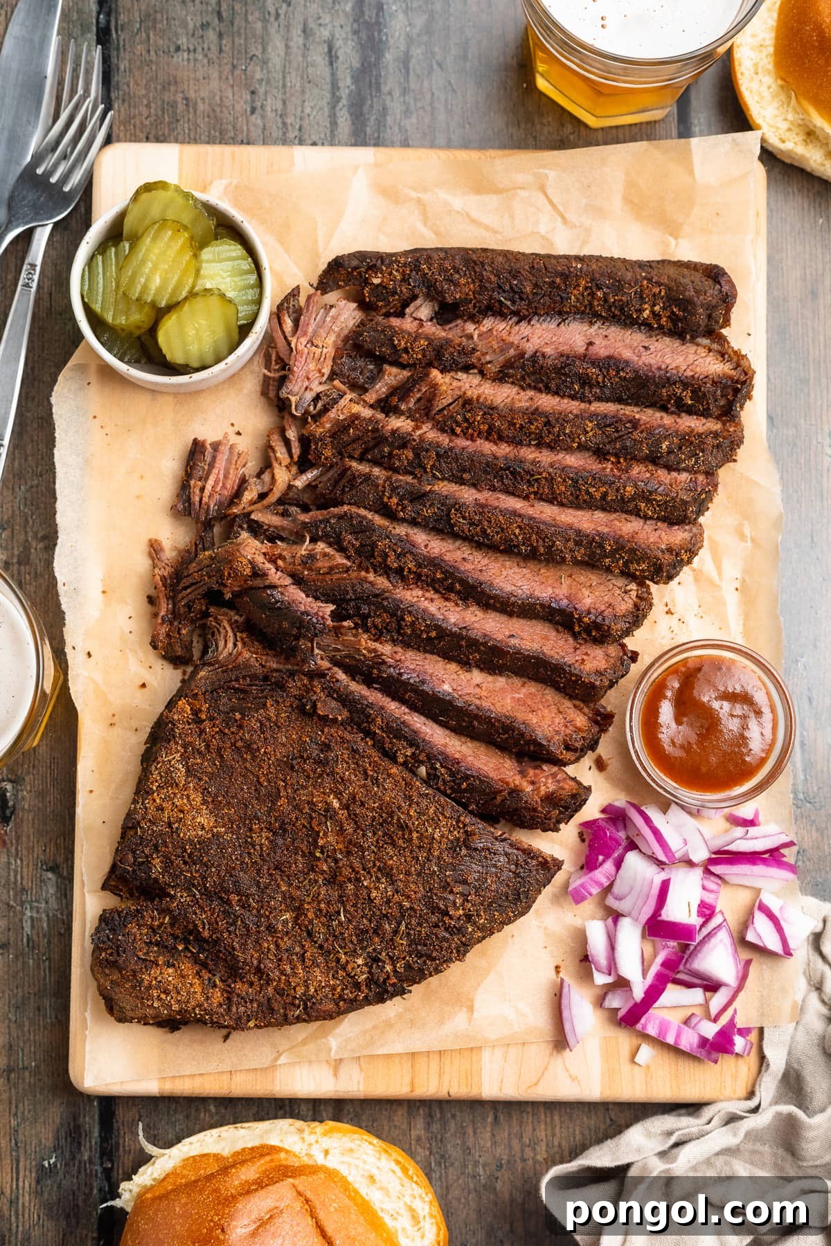 Sous vide brisket, sliced thin and arranged on a wooden serving tray with seasoning and garnish.