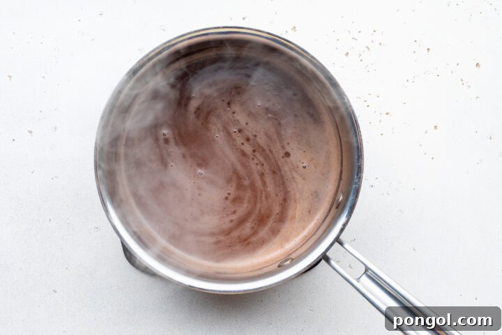 Overhead view of au jus mixture in a silver saucepan on a white countertop.