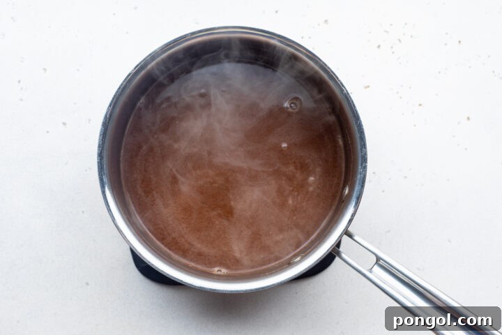 Overhead view of au jus mixture in a silver saucepan on a white countertop.