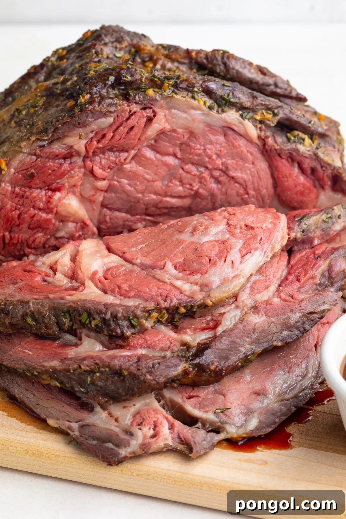 Close-up look at a carved sous vide prime rib on a wooden cutting board in front of a white background.