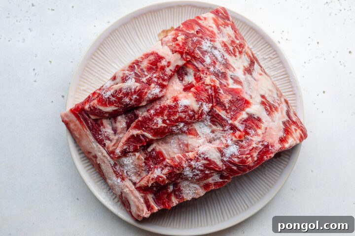 Overhead view of uncooked prime rib seasoned with salt on a round white plate.