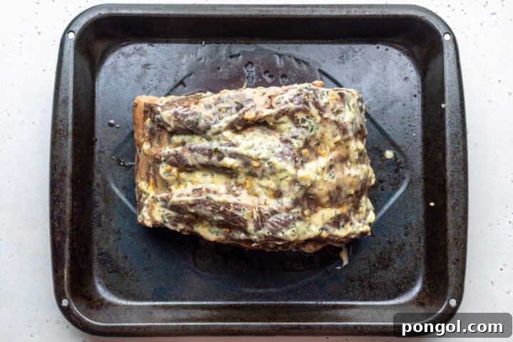 Overhead view of a sous vide prime rib rubbed with seasoned compound butter on a black roasting pan.