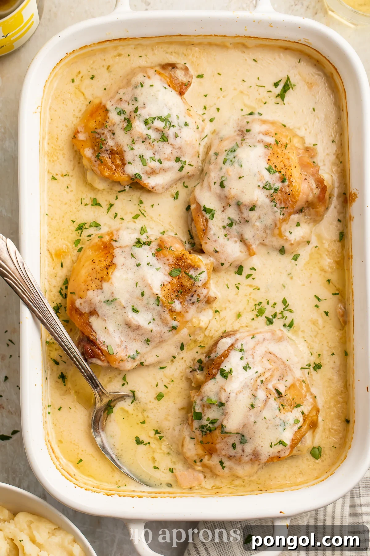 Overhead view of 4 chicken thighs in a large rectangular casserole dish with a spoon resting in a sauce of cream of chicken soup and milk.