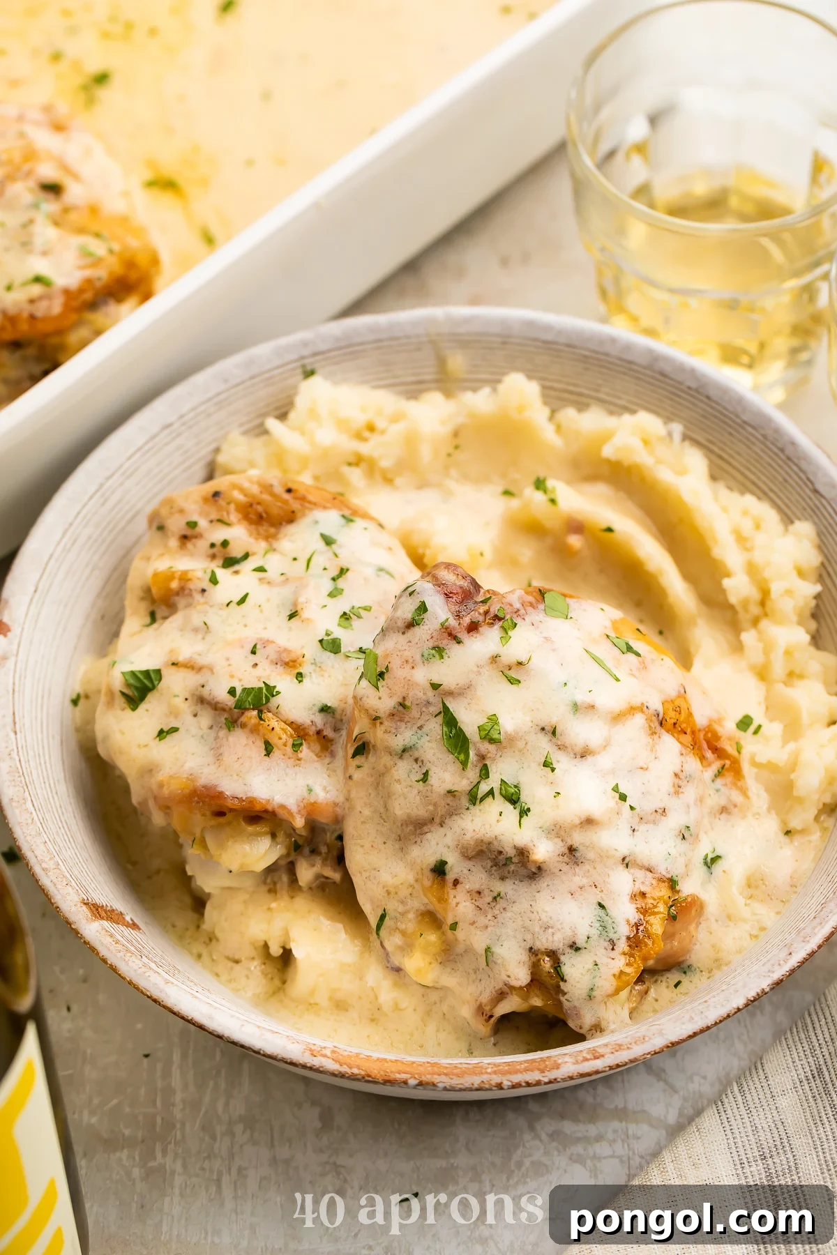 Angled view of a bowl of chicken soup chicken over a bed of creamy mashed potatoes, with a casserole dish of chicken in the background.