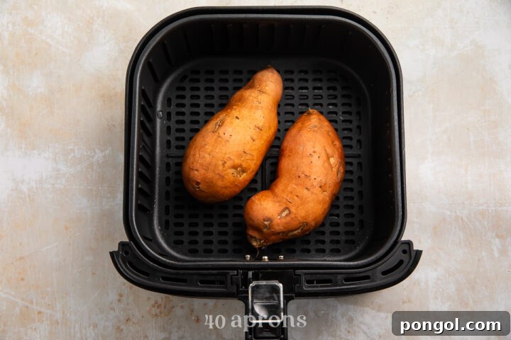 Crispy Air Fryer Sweet Potatoes 6 Overhead view of two medium sweet potatoes in a black air fryer basket on a neutral countertop.