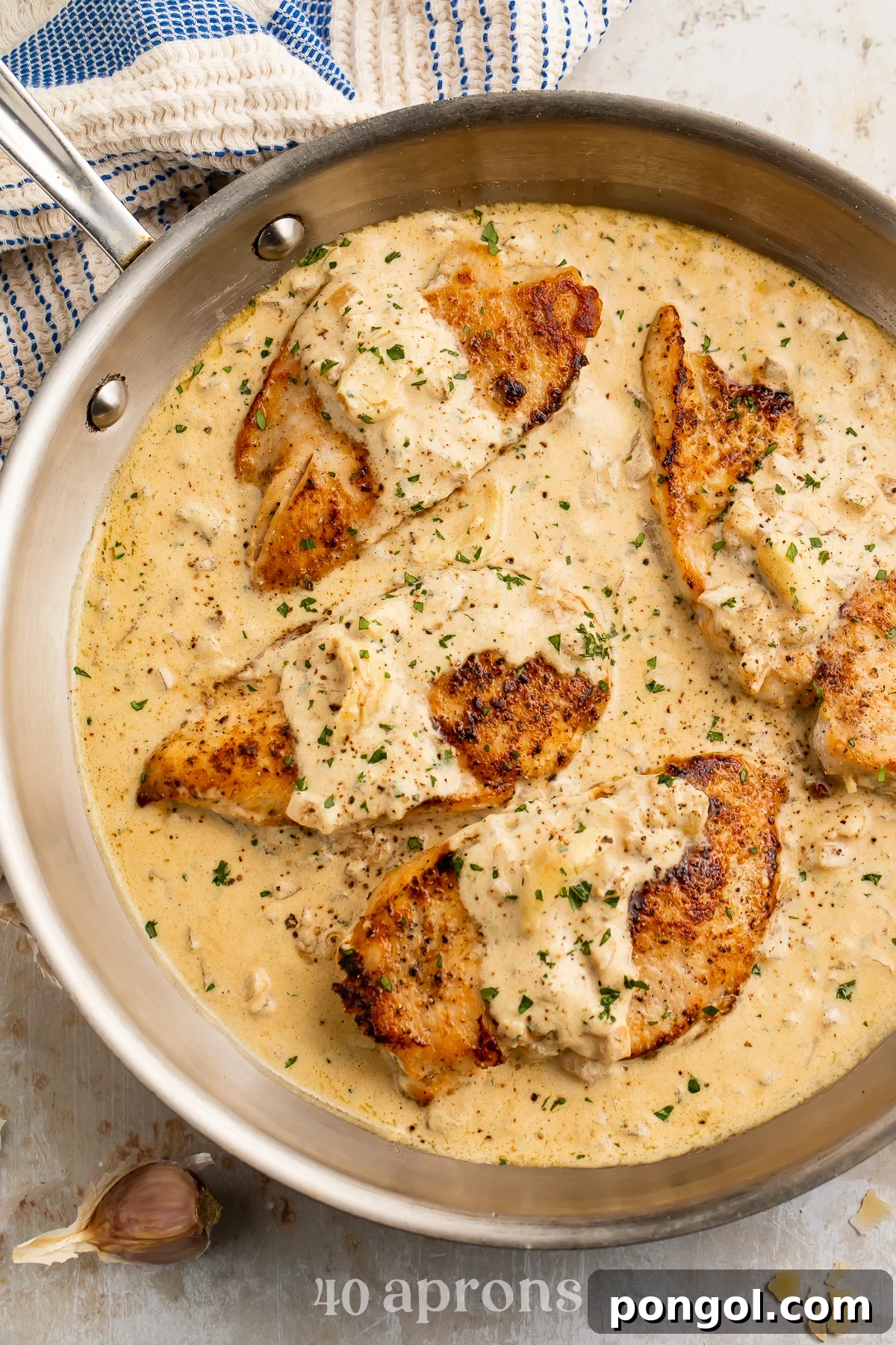 Overhead view of 4 chicken breasts in a creamy garlic sauce in a large silver skillet, ready to be served.